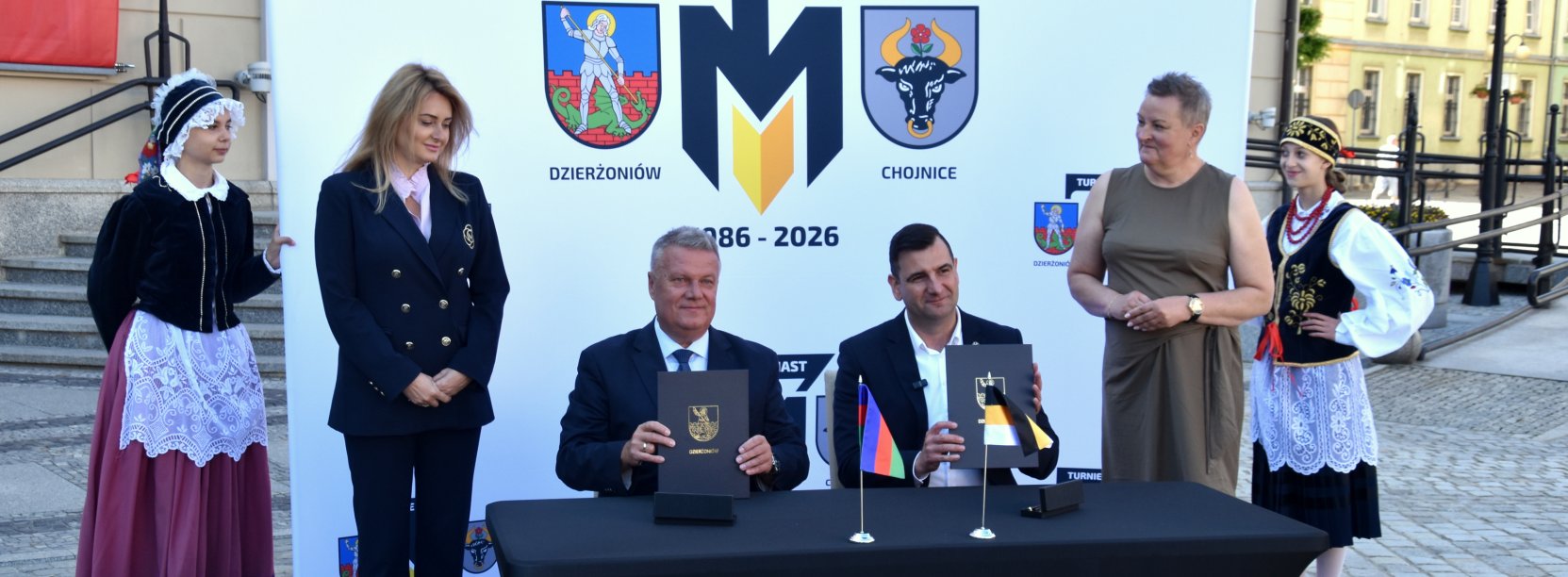 Burmistrz Dzierżoniowa i Chojnic siedzą przy stole, trzymają pospisane umowy