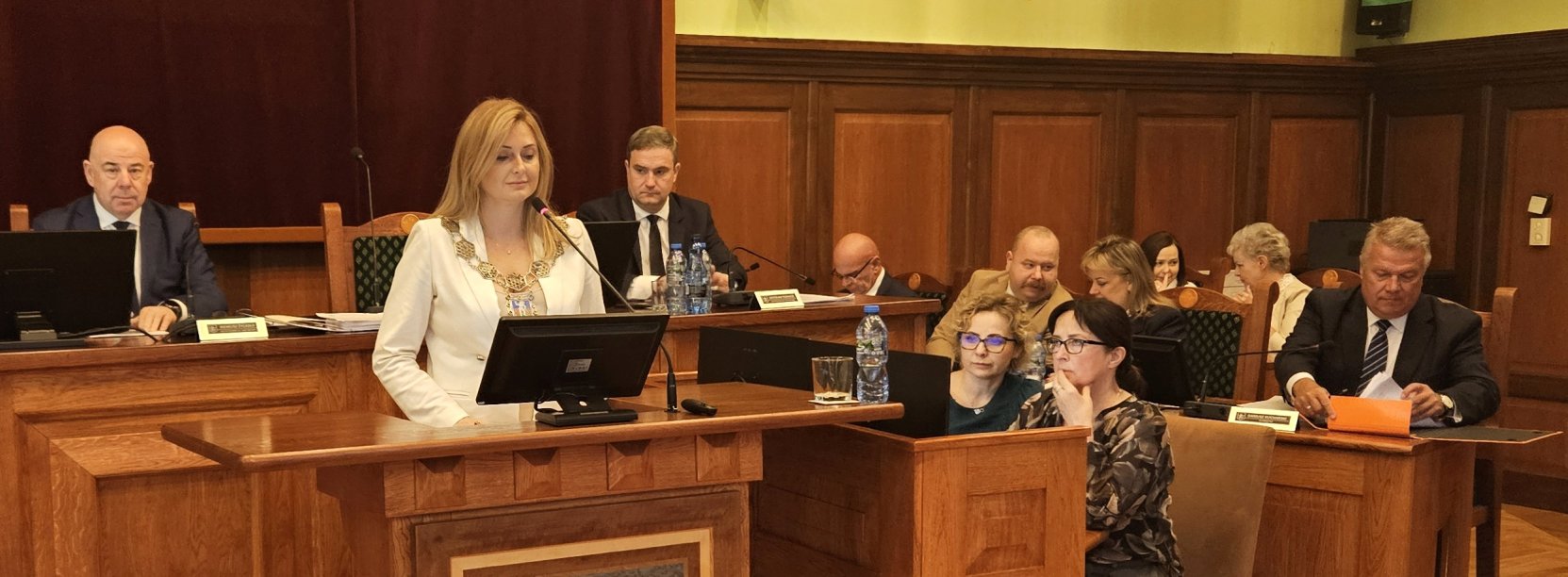 Przewodnicząca rady przy mównicy, za nią przy stole dwóch wiceprzewodniczących, po prawej burmistrz