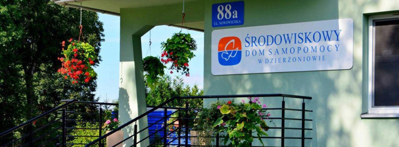 Wejście po schodach prowadzące tarasem do budynku, na ścianie napis Środowiskowy Dom Samopomocy