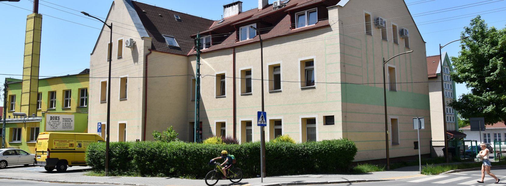 Trzypiętrowy budynek ze spadzistym dachem i piaskowym kolorem elewacji