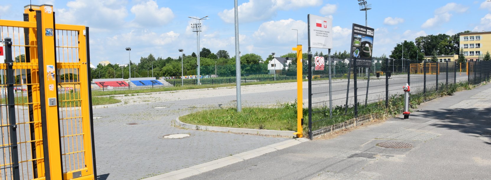 Żółta, otwarta brama przed dużym parkingiem z kostki betonowej