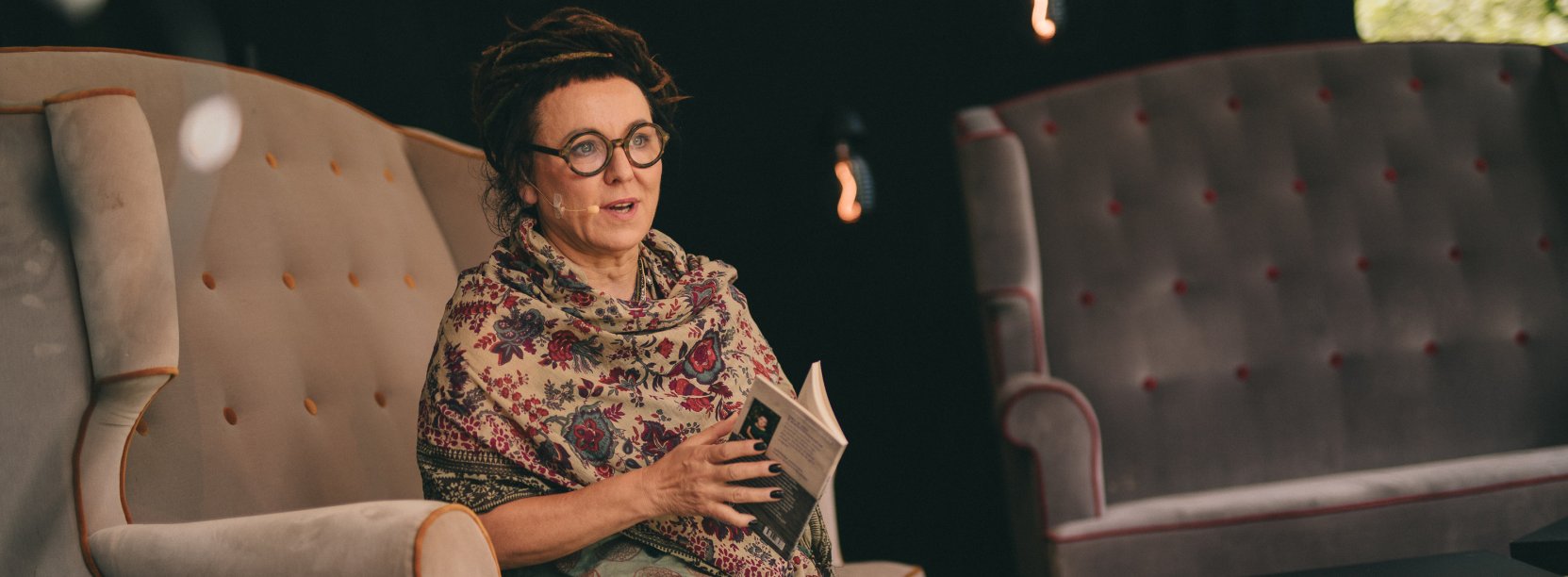 Olga Tokarczuk siedząca w duzym fotelu z książką w rękach