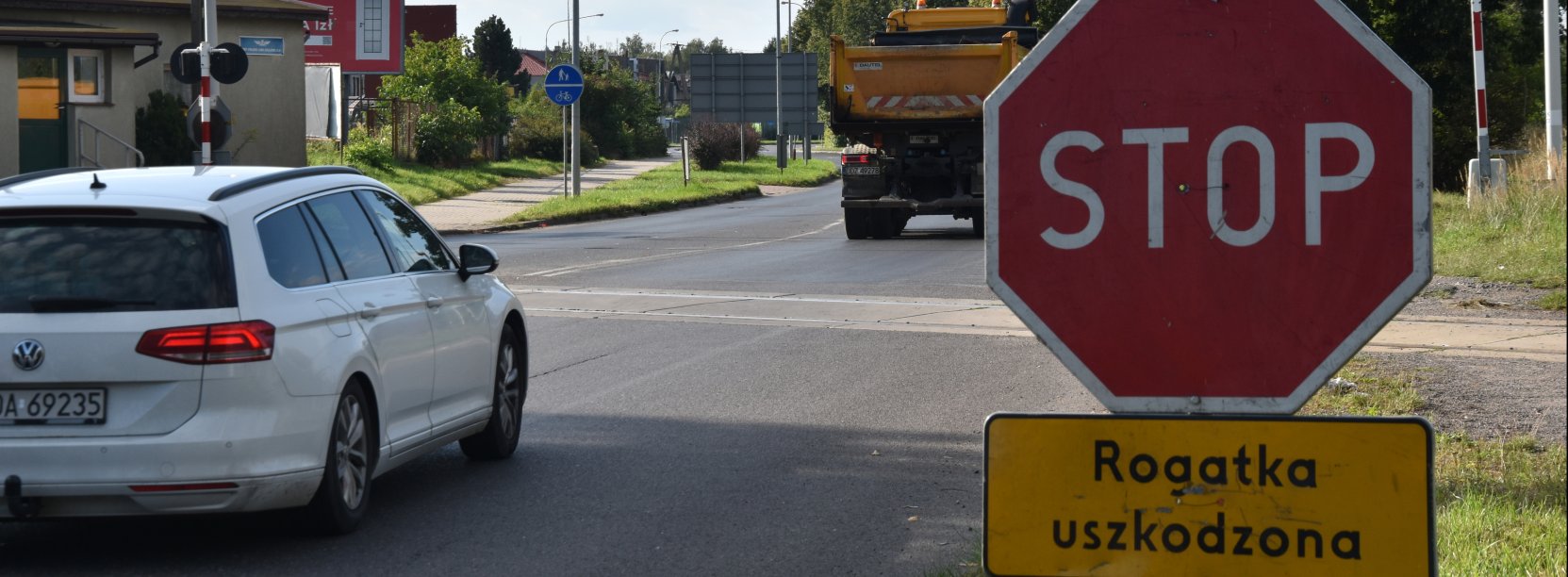 Biały samochód przed przejzadem kolejowy, po prawej znak "Stop"