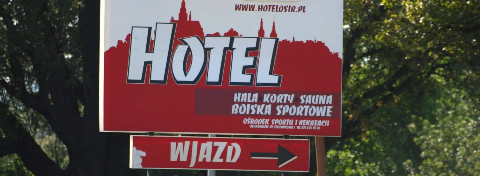 Duży baner przy drodze dojazdowej do ośrodka sportu z napisem hotel