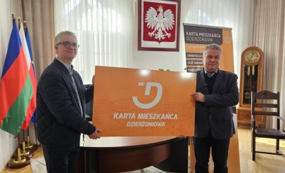 Mieszkaniec dzierzoniowa oraz burmistrz trzymają duża plastikową pomarańczową kartę meiszkańca