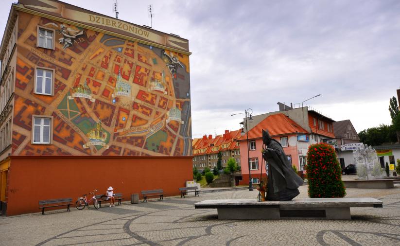 Widok na kamienicę przy ul. Świdnickiej, na której jest mural przedstawiający mape starmiejskiego centrum, po prawej stronie pomnik Jana Pawała II