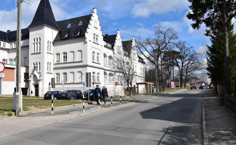 Duża biała kamienica, po prawej stronie drogi drzewa