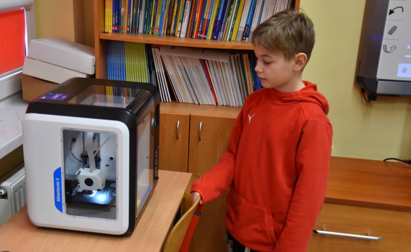 Chłopiec w czerwonej bluzie stojący przed drukarką 3D
