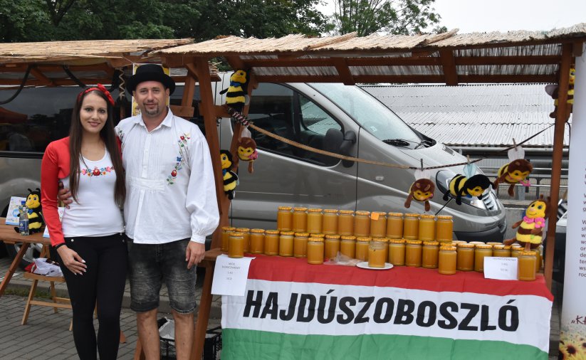Kobieta i mężczyzna przy stoisku z miodami, przed stoiskiem napis Hajduszoboszlo