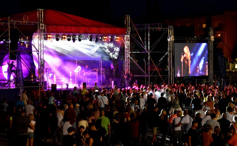 Tłum ludzi przed sceną podczas nocnego koncertu, obok oświetlonej sceny duży ekran