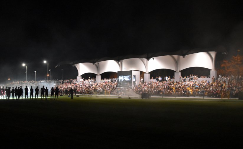 Stadionowa trybuna w nocy pełbna kibiców, częśc trybuny zadaszona i oświetlona