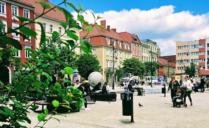 Rynek wyłożony kamienną kstką, po lewej zieleń, w tle kamienice