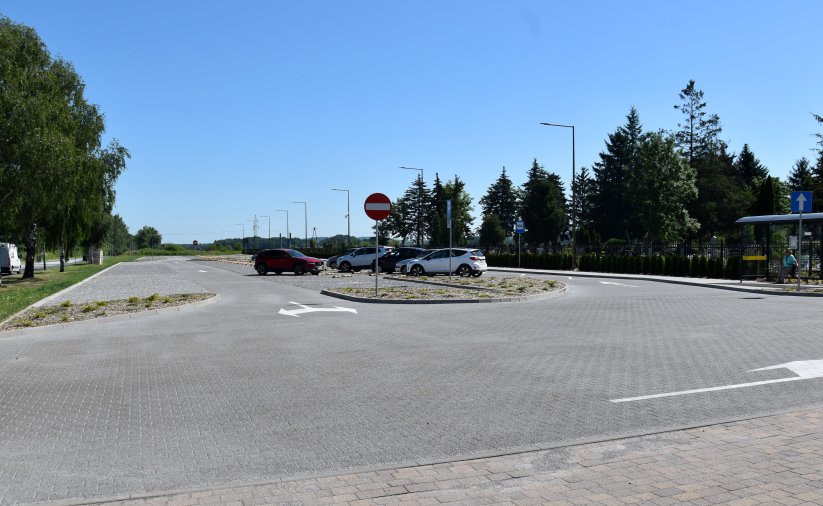 Wjazd na parking i parking przy cmentarzu, po bokach zieleń