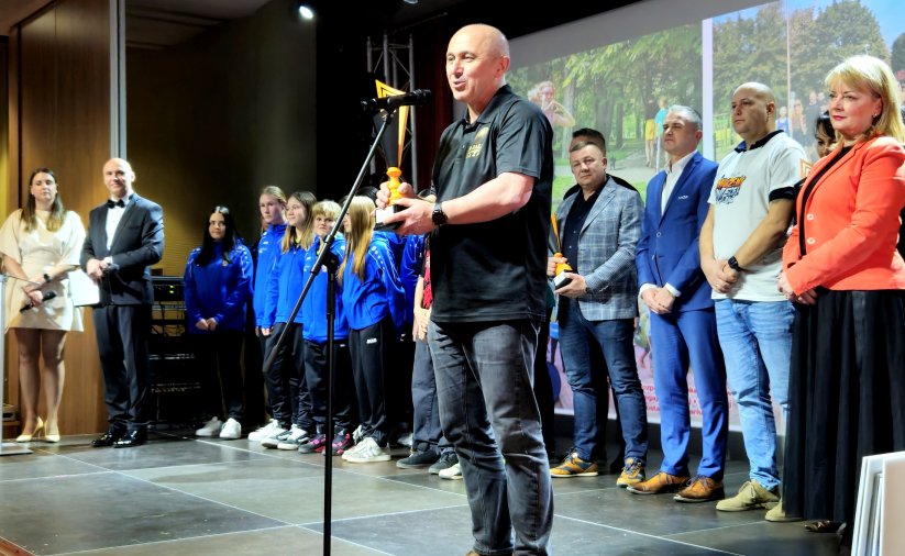 Scena pełna ludzi, przy mikrofonie mężczyzna