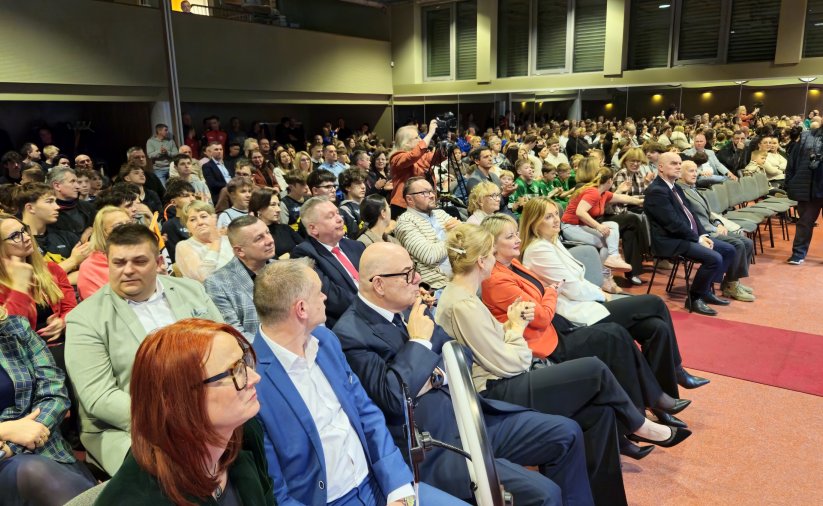 Widownia wypełniona ludźmi siedzącycmi na krzesłach