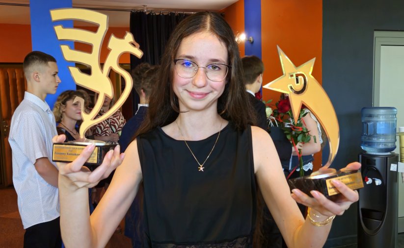 Uśmiechnięta uczennica trzymająca dwie statuetki