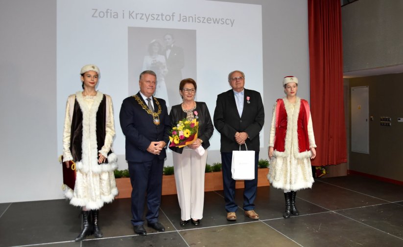 Para małżeńska wyrózniona medalem na zdjęciu z burmistrzem i dwiema dziewczynami w ludowych strojach