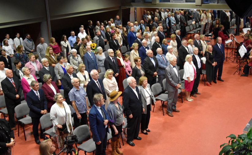Uczestnicy wydarzenia stoją podczas śpiewania hymnu Polski