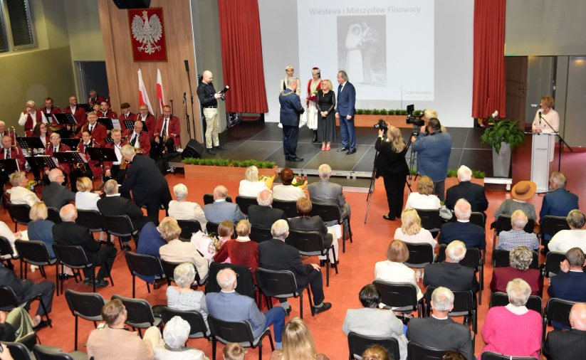Uroczystość wręczenia medali z góry, pary siedzą na krzesłach, na scenie burmistrz