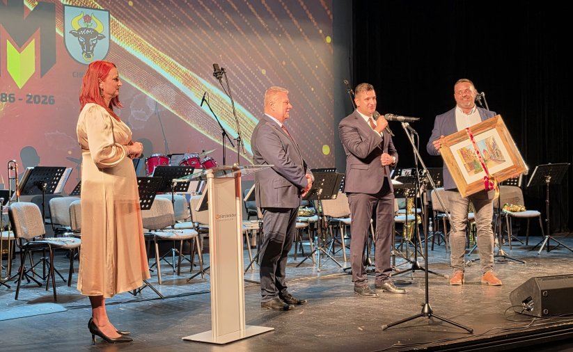 Burmistrz Dzierzoniowa i burmistrz Chojnic trztymający duży obraz na scenie kinoteatru