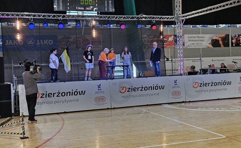 grupka zawodników grająca w jengę na scenie ustawionej w hali sportowej