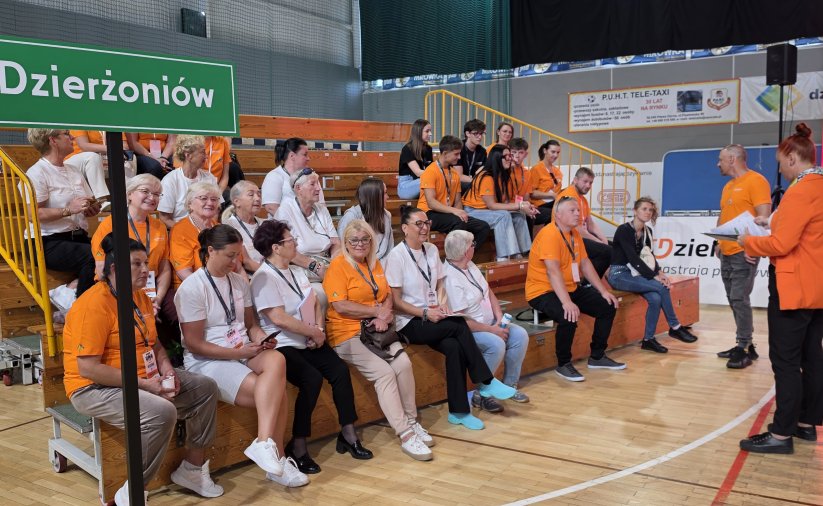 Kibice na małej trybunie w hali sportowej, większość w pomarańczowych koszulkach