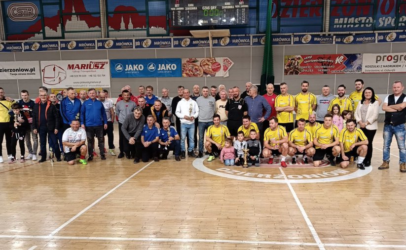Kilkadziesiąt osób na wspólnym zdjęciu wewnątrz hali sportowej, częśc w żółtych strojach