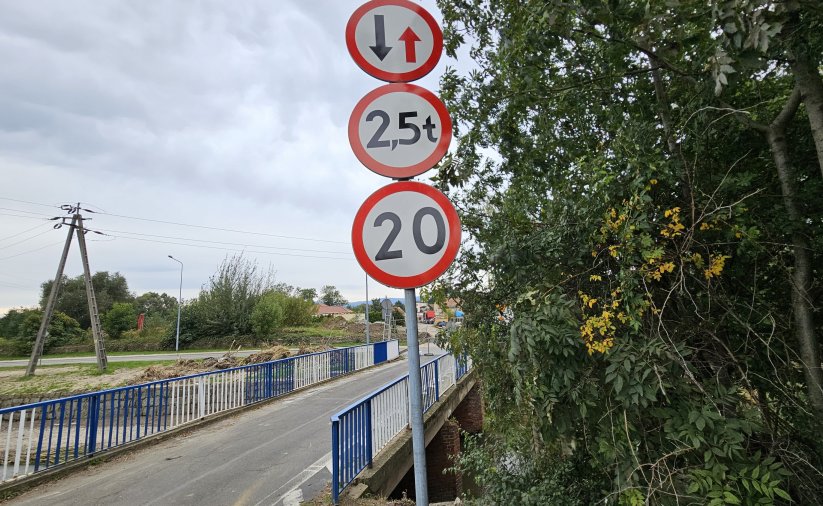 Mały most, po bokach biało-niebieski barierki, przed mostem znak ograniczenia prędkości do 20 km/h i ograniczenia wjazdu aut powyżej 2,5 tony 
