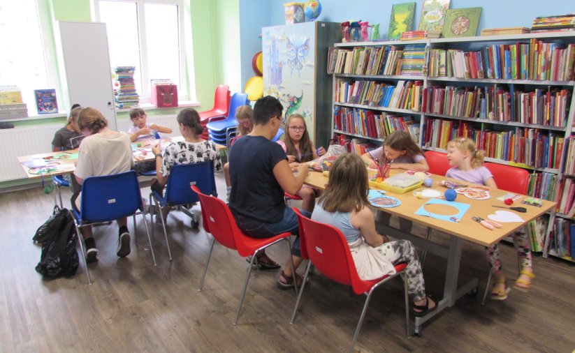 Grupa dzieci maluje przy dwóch stołach w bibliotece