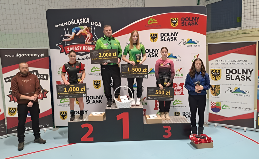 Zapaśniczki stojące na podium z symbolicznymi czekami