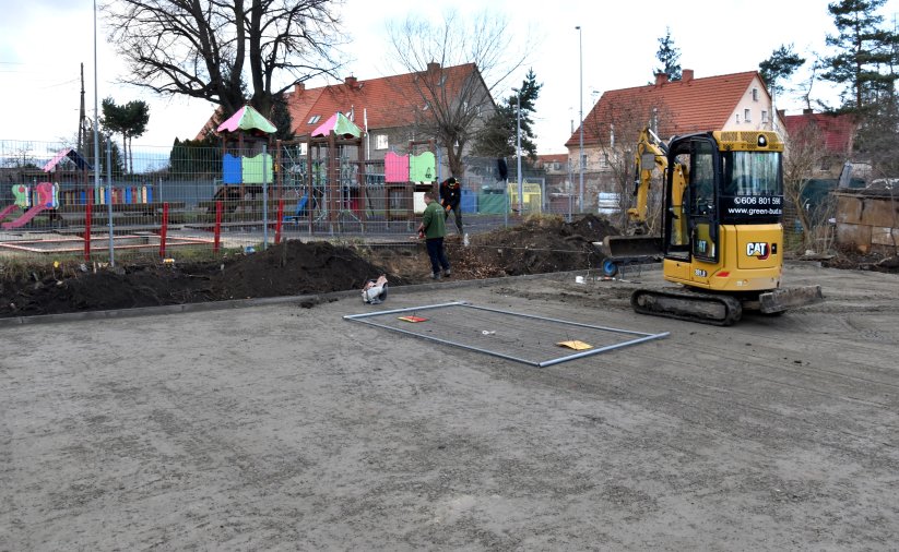Utwardzony teren pod boisko do koszykówki, w tle plac zabaw i budynki mieszkalne