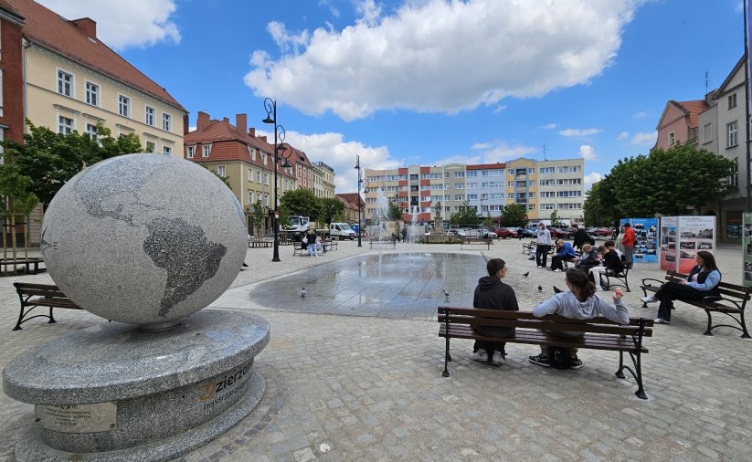 Rynek, ludzie siedzący na ławkach, po lewej ogromny kamienny globus