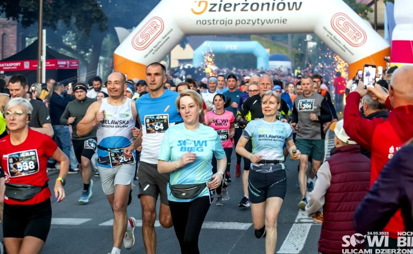 Ulica zapełniona biegaczami w sportowych strojach, za nimi napis Dzierżoniów