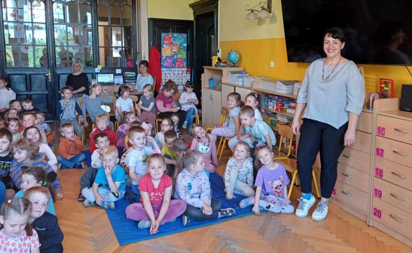 Grupa przedszkolaków siedzących na podłodze w dużym pomieszczeniu