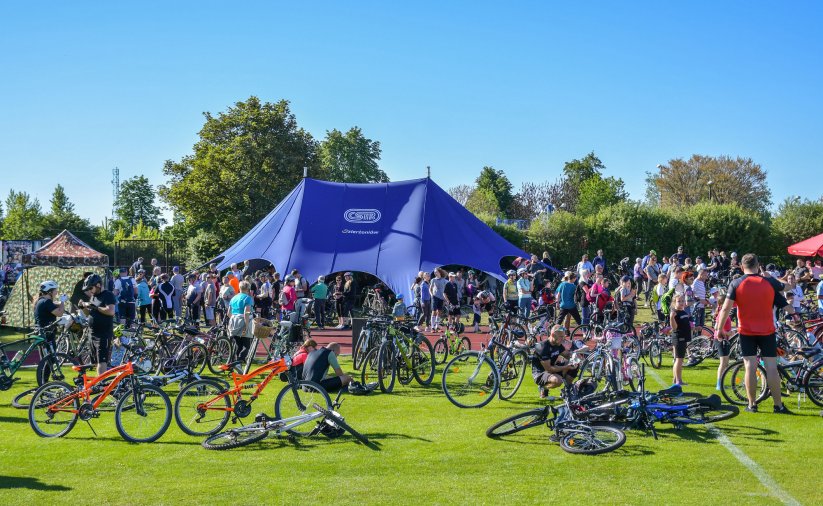 Kilkudzisięciu rowerzystów przy dużym niebieskim namiocie