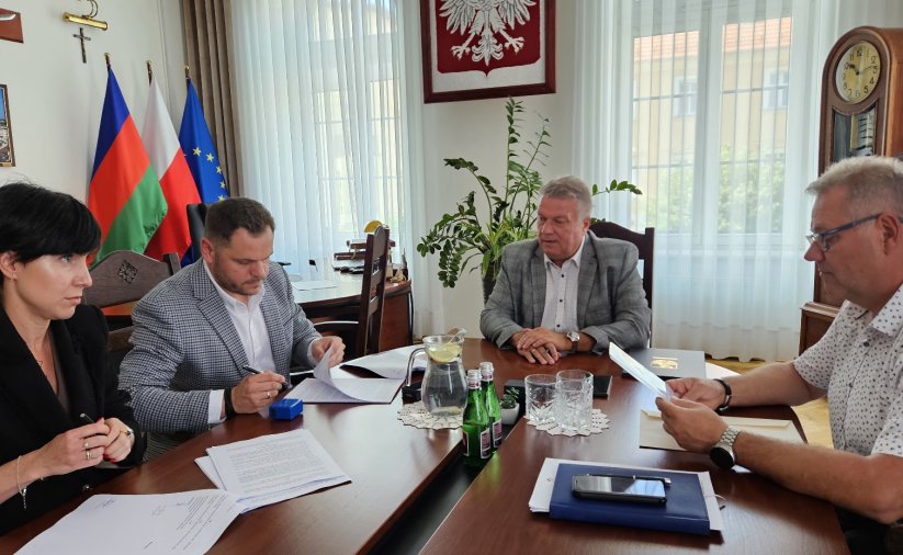 Cztery osoby, w tym burmistrz miasta Dariusz Kucharski (w środku), podpisują dokumenty przy stole w gabinecie burmistrza Dzierżoniowa
