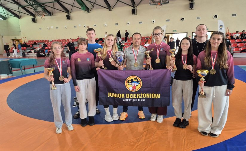 grupa 5 zapaśniczek z medalami i pucharami z trenerami i flagą klubu sportowego Junior Dzierżoniów