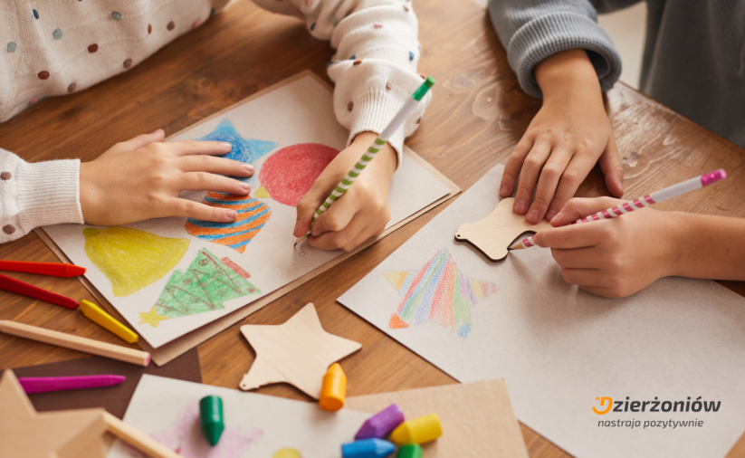 Ręce siedzących przy stole dzieci rysujących świąteczne elementy na kartkach papieru