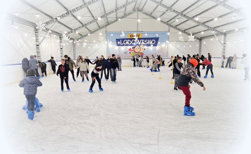 Wnętrze namiotu z lodowiskiem, na tafli lodowiska łyżwiarze w różnym wieku