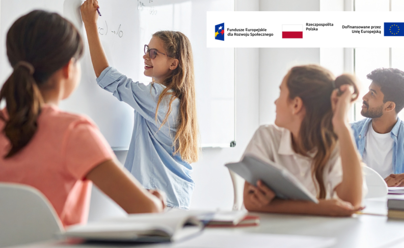 Grupa uczniów w klasie, jedna z uczennic pisze po tablicy