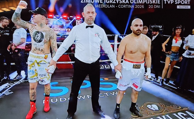 Ring bokserski, po wygranej walce dwaj bokserzy z sędzią, Kamil Bednarek unosi zaciśniętą rękę do góry w geście zwycięstwa