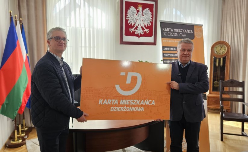 Mieszkaniec dzierzoniowa oraz burmistrz trzymają duża plastikową pomarańczową kartę meiszkańca