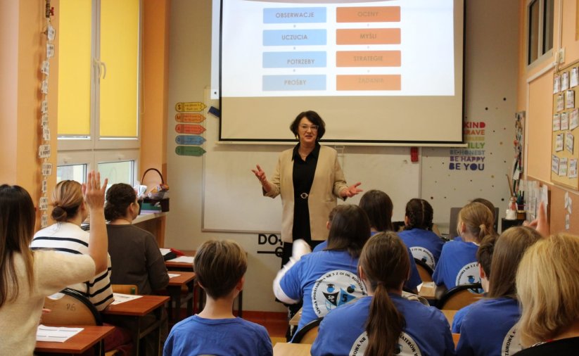 Uczniowie w ławkach przy tablicy kobieta prowadząca zajęcia