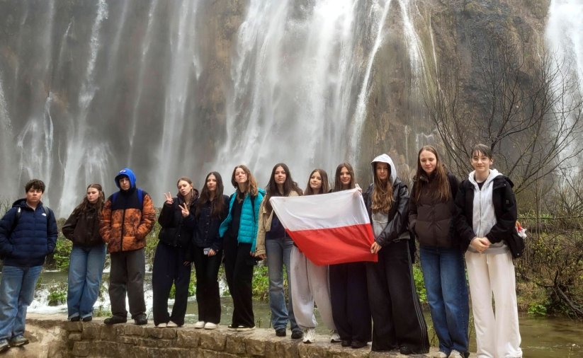Uczniowie na wspólnym zdjęciu z flagą Polski, na drugim planie wodospad