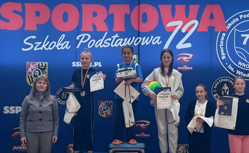 Pięć zawodniczek, trzy stoją na podium, dwie obok, niebieskie tło