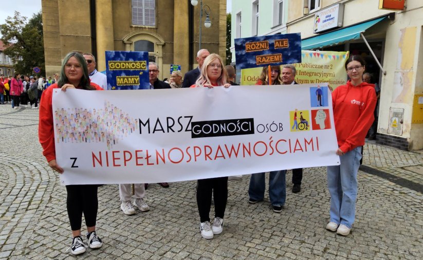 Trzy dziewczyny trzymające baner z napisem "Marsz osób z niepełnosprawnościami"