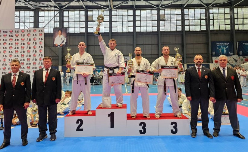 Czwórka zawodników w strojach do karate stoi na podium. Na najwyższym stopniu Tomasz Staściuk z uniesionym do góry pucharem