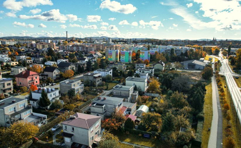 Miasto z góry, na pierwszym planie domki jednorodzinne, za nimi osiedla, dalej góry 