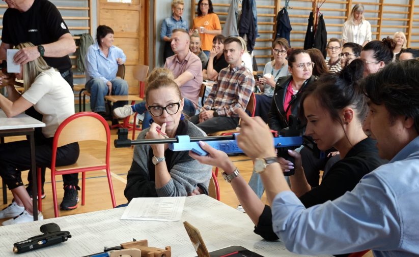 Szkolenie, wypełniona sala gimnastyczna, na pierwszym planie instruktor i kobieta trzymająca karabin