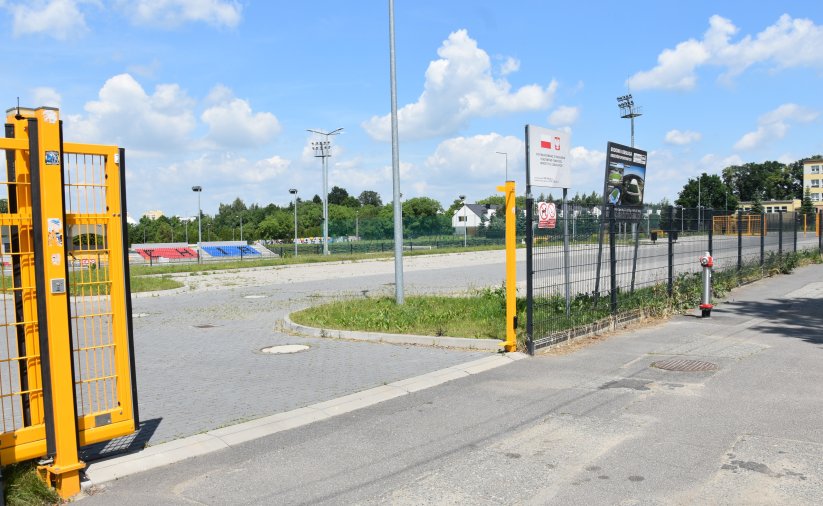 Żółta, otwarta brama przed dużym parkingiem z kostki betonowej